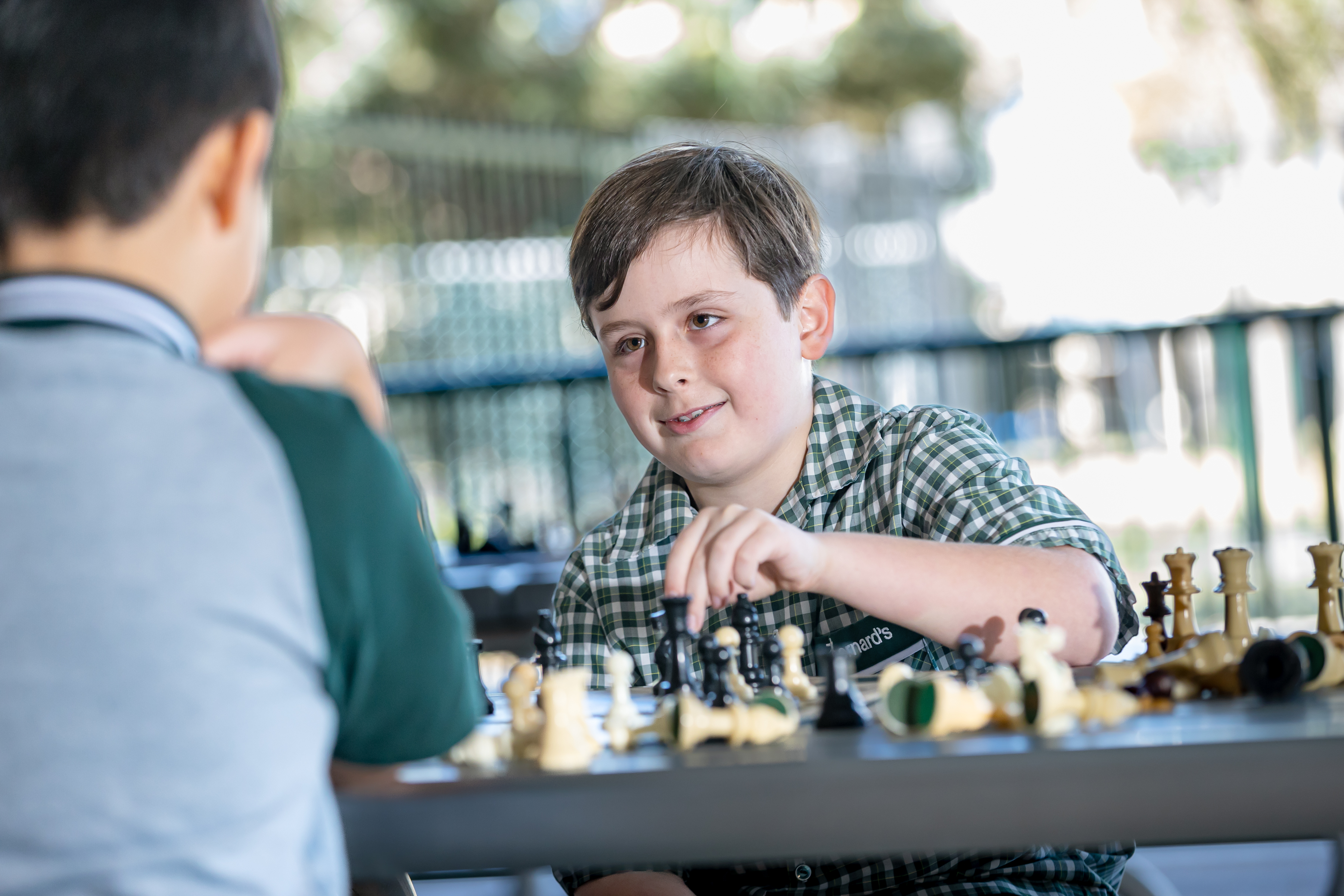 Student playing chess at a table with another student, moving a piece during a game.