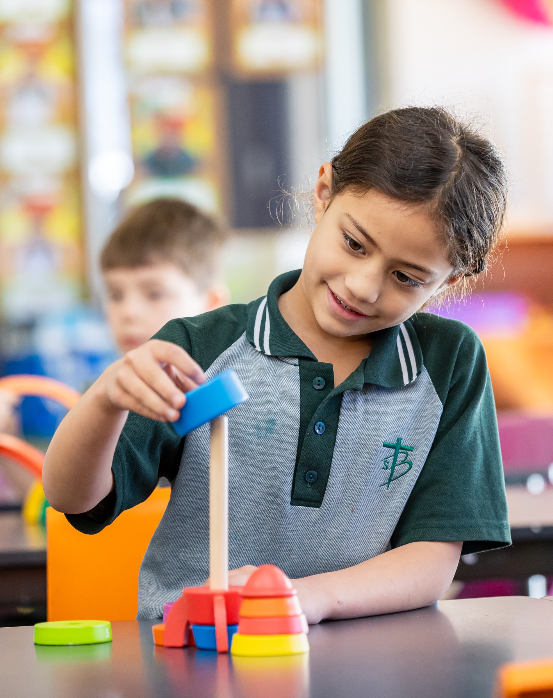 Child placing a blue ring onto a stacking toy at a classroom table.