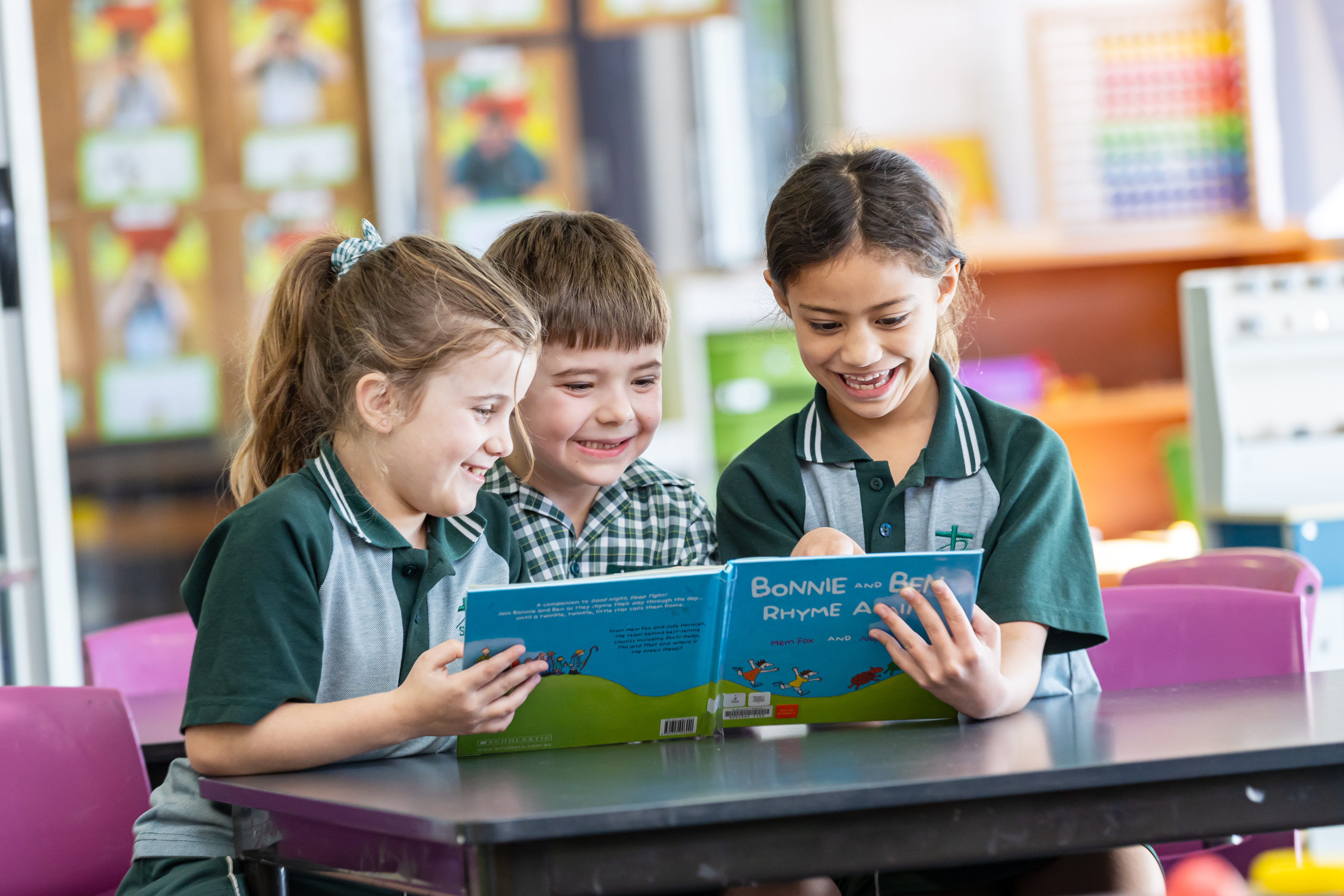 Three students sitting at a table reading a picture book together.
