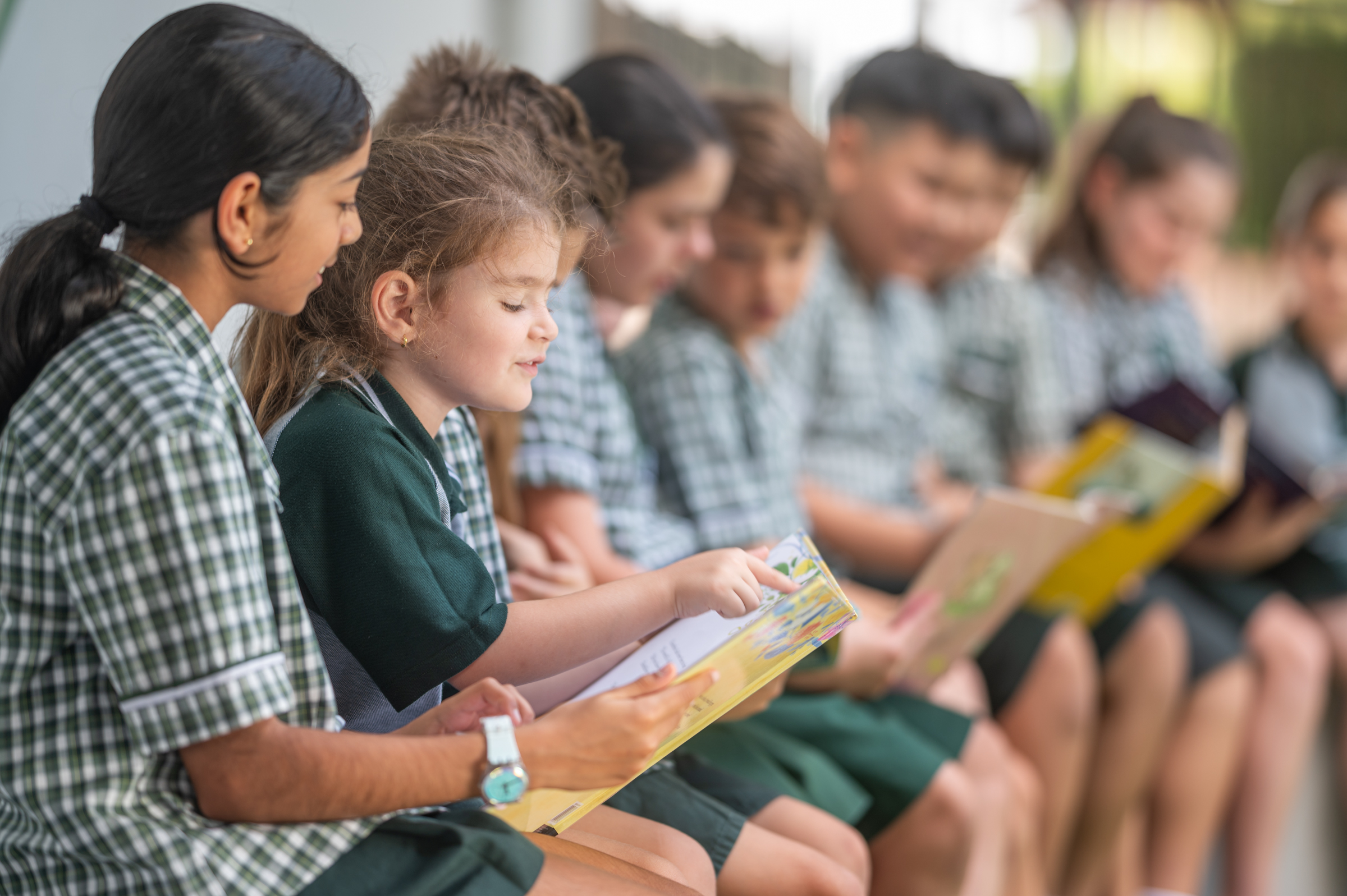 Group of students seated together reading books, with one student pointing to a page while another looks on.