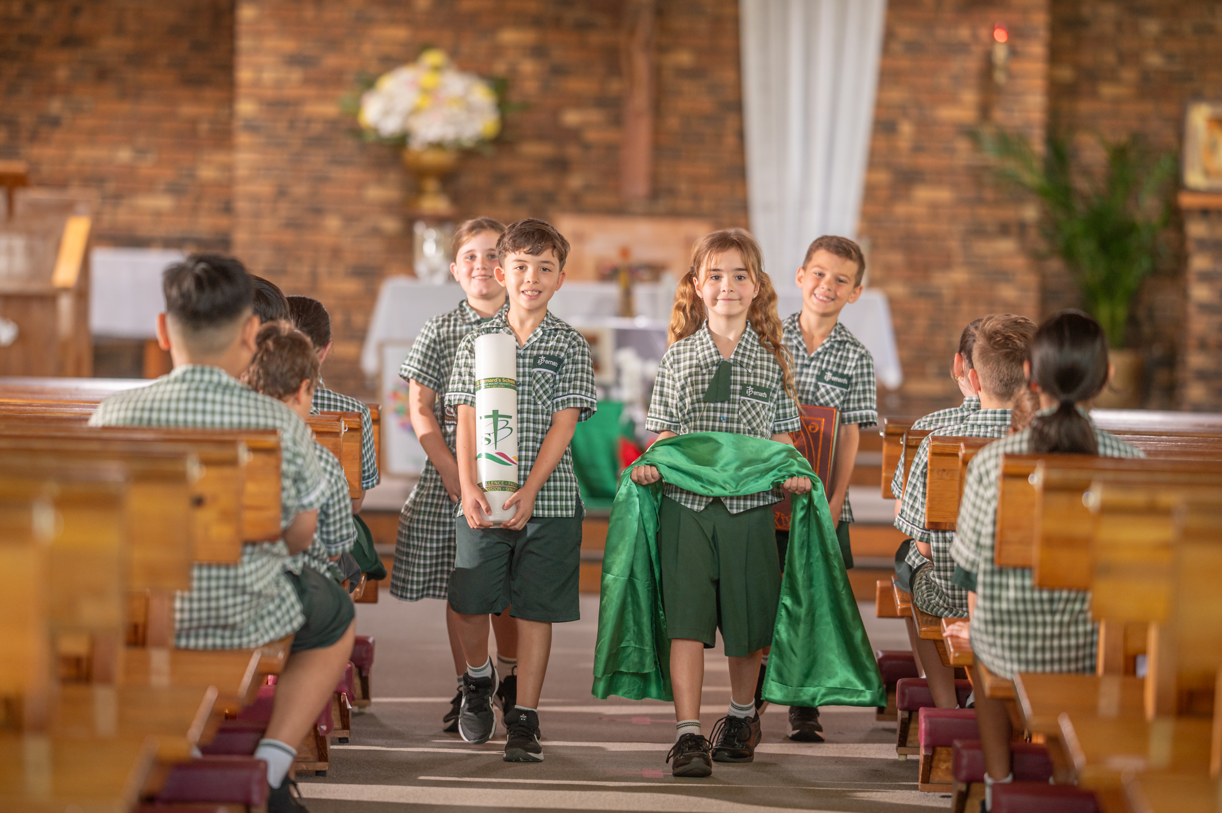 Students in uniform walking down a church aisle carrying a candle and cloth.