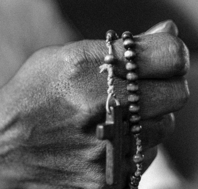 Blak and white picture of a hand holding rosary beads.