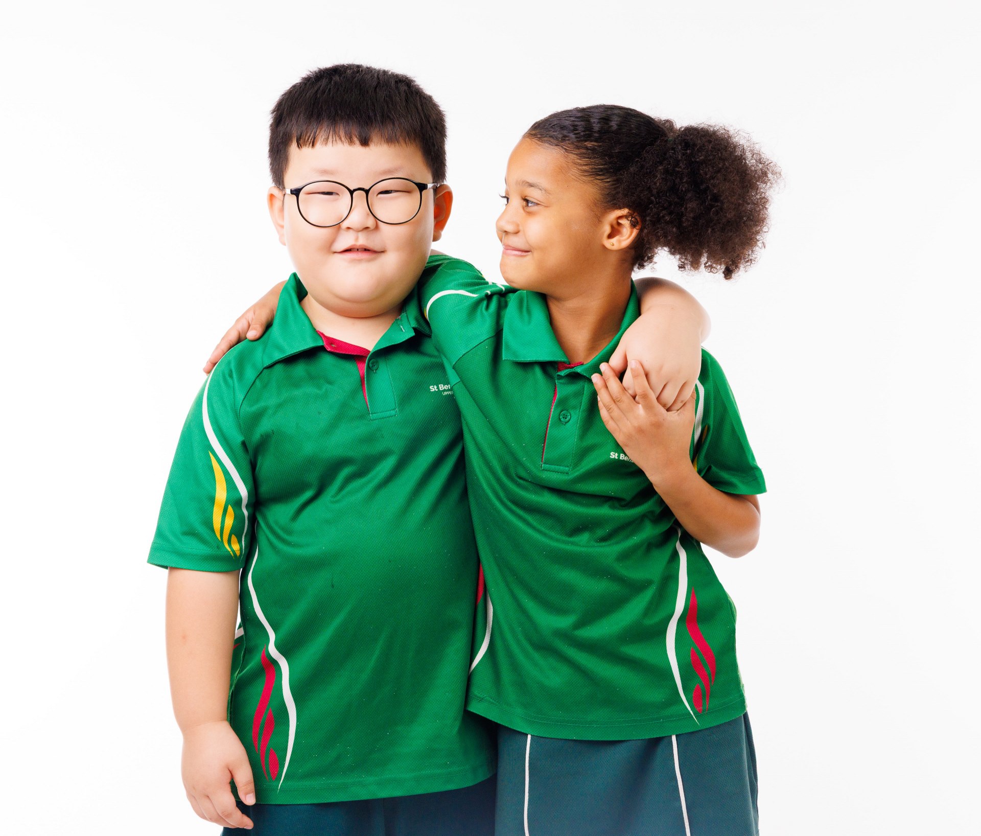 Two students in green sports uniforms standing side by side, with one student’s arm around the other against a plain background.