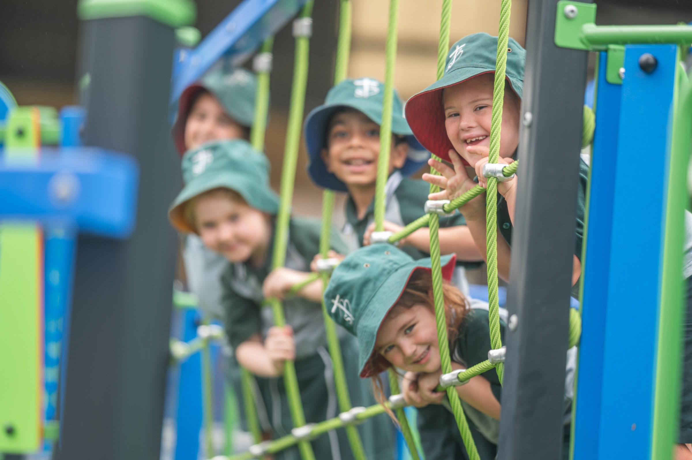 Children in school uniforms climbing and holding onto ropes on playground equipment outdoors.